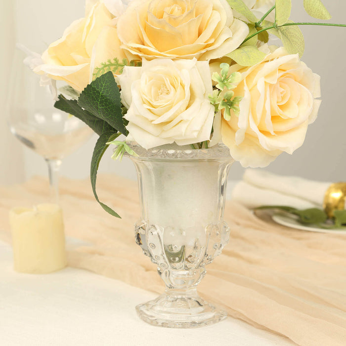 Glass vase with yellow roses and greenery on a table.