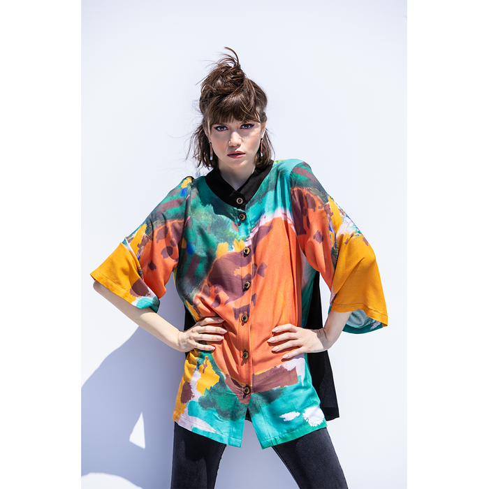 A model wearing a colorful abstract print top with 3/4 sleeves and a button-up front, standing against a plain background.