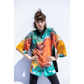 A model wearing a colorful abstract print top with 3/4 sleeves and a button-up front, standing against a plain background.