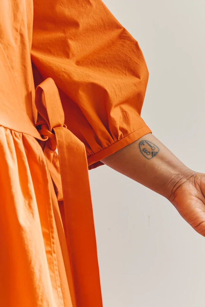 Person wearing an orange malie Wrap Dress made with PDF sewing pattern  with a plain background