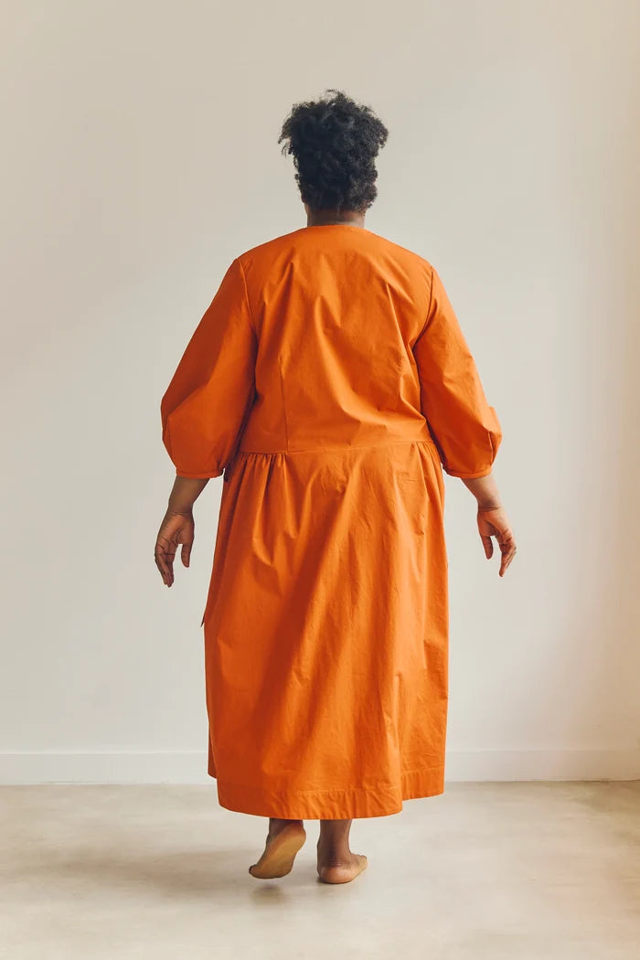 Person wearing an orange malie Wrap Dress made with PDF sewing pattern standing against a plain background