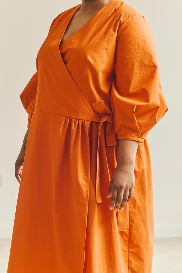 Person wearing an orange malie Wrap Dress made with PDF sewing patternagainst a plain background