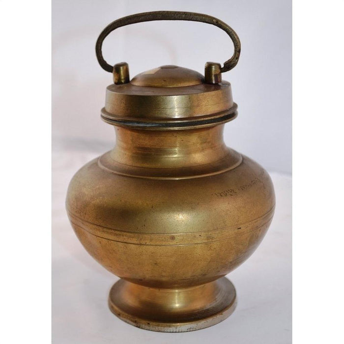 Close-up of antique brass milk jar with lid and handle, hand casted, set against plain white background.