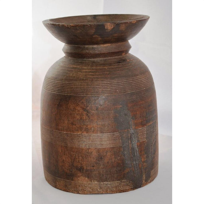 Close-up of rustic brown antique Indian milk storage container with carved lines and wide rim on a light background.