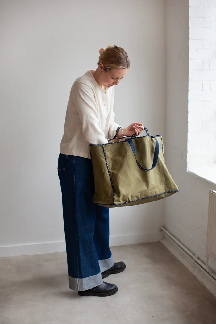 Person holding a green bag made using the Away Tote PDF Sewing Pattern  in a minimalistic room with white walls and a radiator.