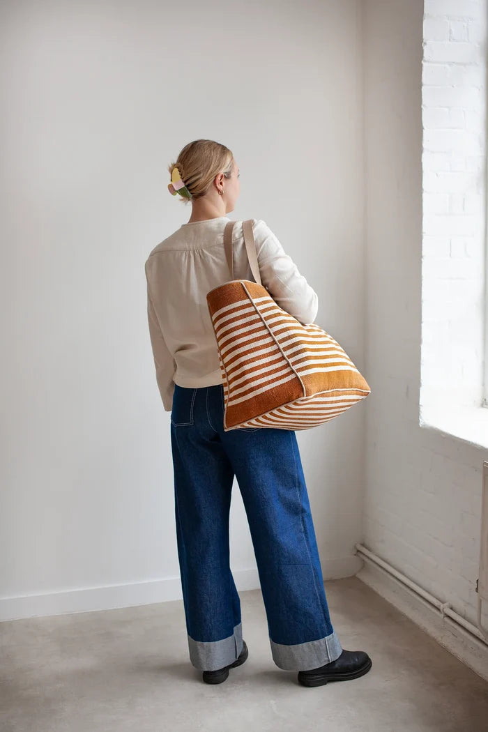 Person holding a striped bag made using the Away Tote PDF Sewing Pattern  in a minimalistic room with a window.