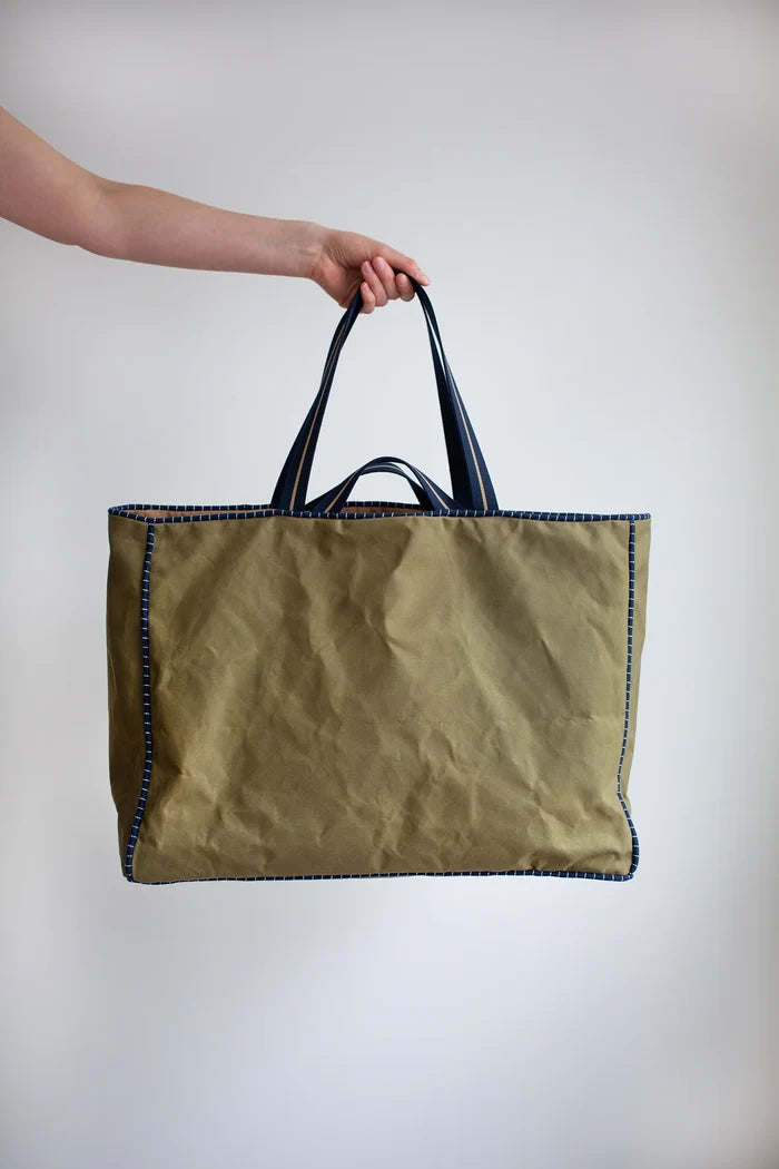 Person holding a green tote bag with black handles made using the Away Tote PDF Sewing Pattern  against a plain background