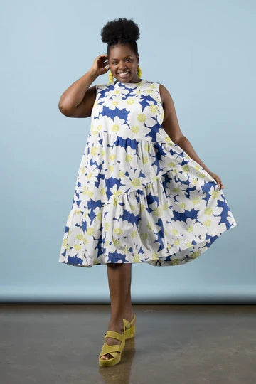 Woman wearing a blue and white floral dress made using Azure Dress, Skirt, and Top sewing pattern against a light blue background