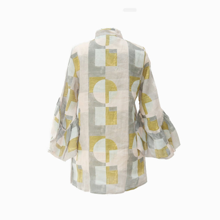 A high neck linen blouse with bell ruffle sleeves, featuring a color blocked geometric pattern in shades of pink, gray, aqua, and blush, with buttons made from smoothed raw coconut shells.