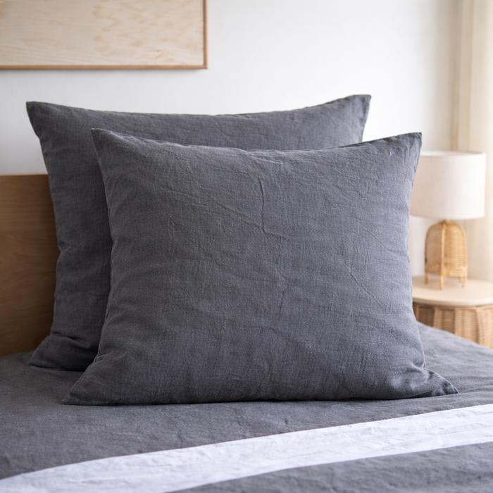 Two Charcoal grey European linen pillows on a bed with a neutral background