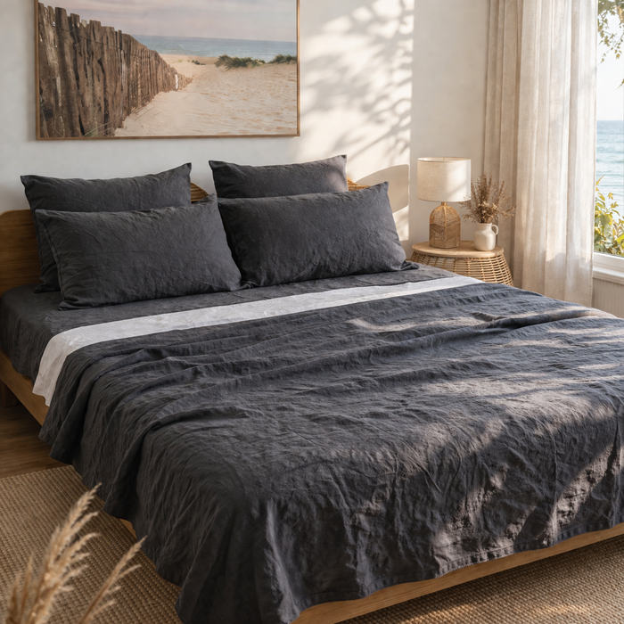 Bedroom with a bed covered in dark gray bedding, a lamp on a bedside table, and a painting on the wall.