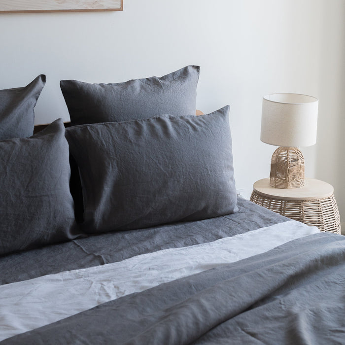 Grey  pillowcases  set on a bed with a lamp and side table in the background.