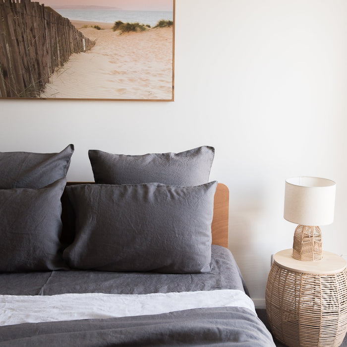 Bedroom with Charcoal grey linen pillowcases  and a lamp on a side table.