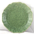 Close-up of a green celadon ceramic plate or bowl with crackled glaze and scalloped edges, against a light background.
