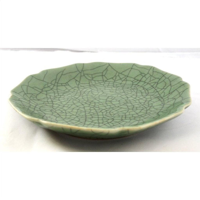 Green celadon ceramic plate or bowl with crackle glaze and scalloped edge, close-up on white surface.
