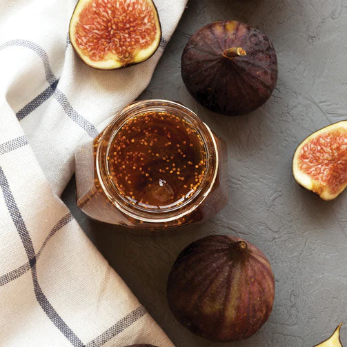 A jar of fig jam next to fresh figs on top of a table