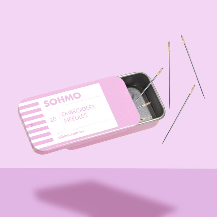 Pink tin box labeled 'SOHMO' with embroidery needles on a pink background