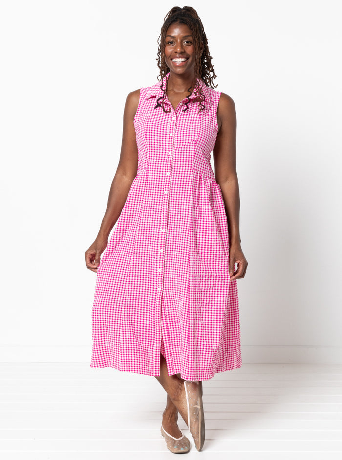 Woman wearing a pink checkered dress on a white background. the dress made using Hampton Woven Dress Sewing Pattern – Mid-calf shirtdress with gathered skirt, curved waist, sleeve or sleeveless options, and inseam pockets.