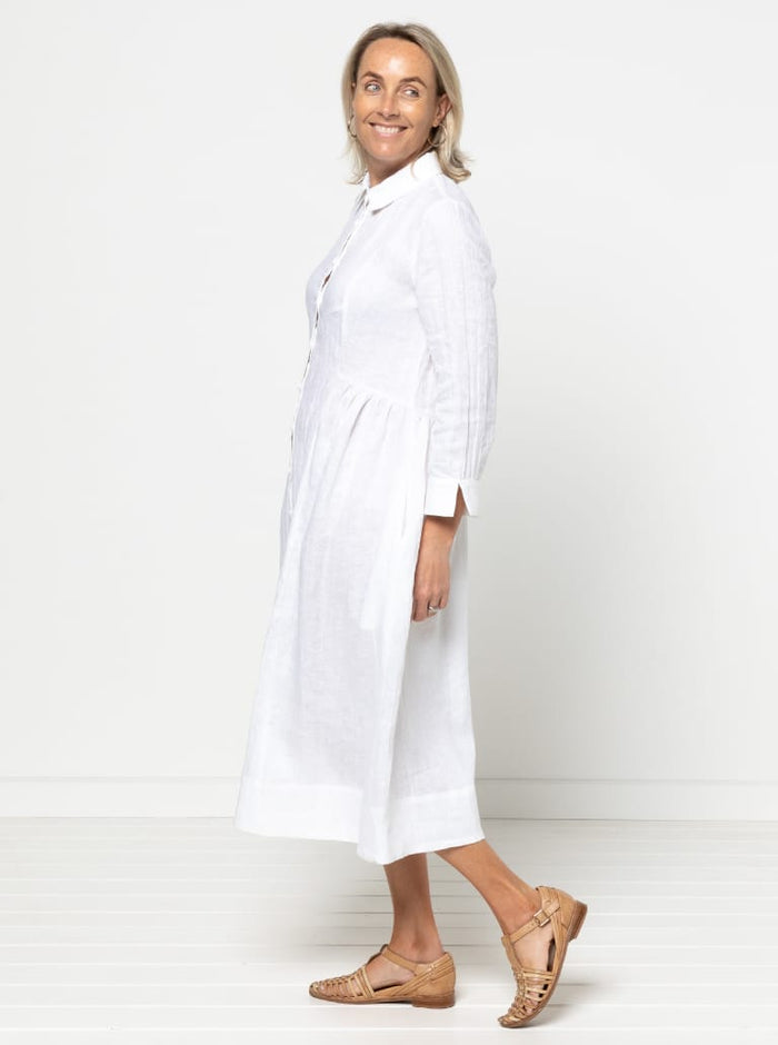 Woman wearing a white dress against a plain background. the dress made using Hampton Woven Dress Sewing Pattern – Mid-calf shirtdress with gathered skirt, curved waist, sleeve or sleeveless options, and inseam pockets.