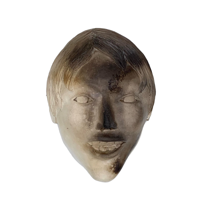 A ceramic sculpture mask depicting a young boy's face, primarily in shades of gray.