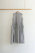 A sleeveless gray and white textured dress with side tie details, hanging on a wooden hanger from a wooden clothing rack against a plain white wall.