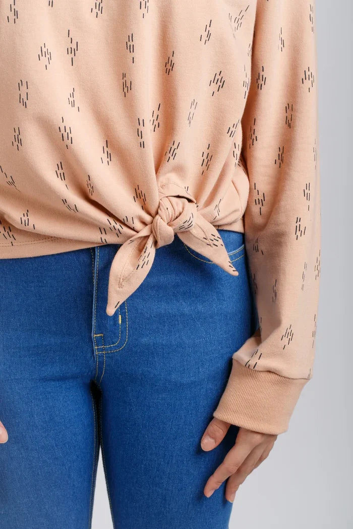 Person wearing a beige patterned Jarrah sweater and blue jeans on a gray background