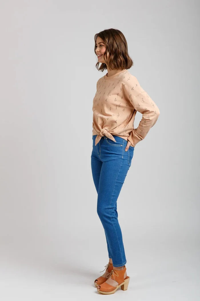 Woman wearing a beige Jarrah sweater and blue jeans on a plain background