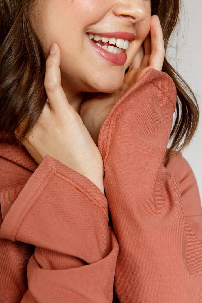 Person wearing a rust-colored Jarrah sweater with a plain background