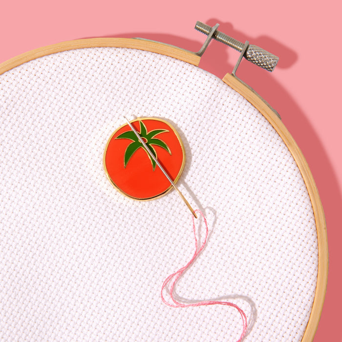 Embroidery hoop with a red circular patch featuring green leaves on a pink background