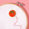 Embroidery hoop with a red circular patch featuring green leaves on a pink background