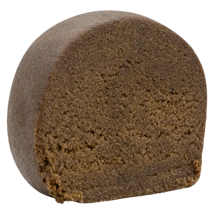 Close-up front view of a dense, dark brown half-cylinder of Montreal-Style Aged Hash showing its crumbly, textured interior.