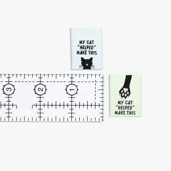 Two small signs with cat-themed text and a ruler for scale on a white background.