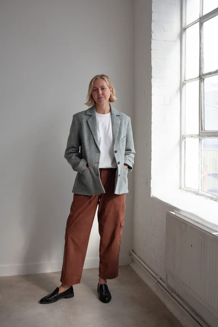 Person wearing a gray blazer made using Naomi Blazer PDF Sewing Pattern  and brown pants standing in a room with a large window.
