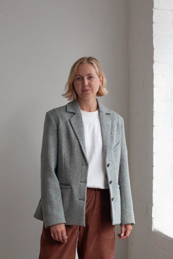Woman wearing a gray blazer made using Naomi Blazer PDF Sewing Pattern  over a white shirt and brown pants against a light gray wall.