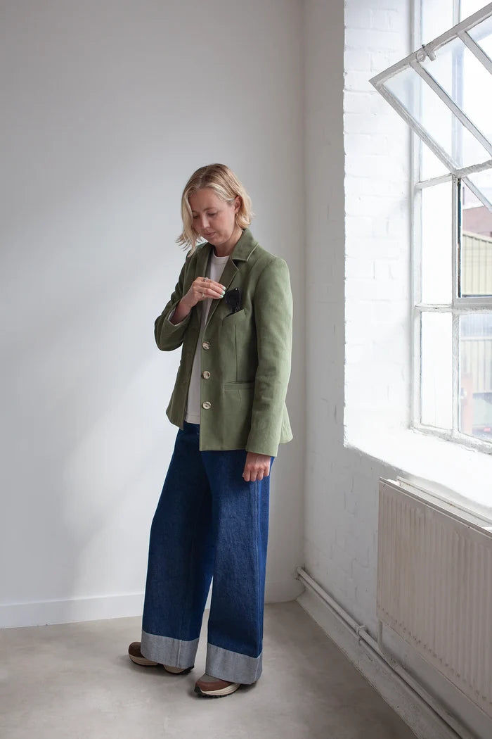 Person wearing a green jacket made using Naomi Blazer PDF Sewing Pattern  and blue pants standing in a room with a window.