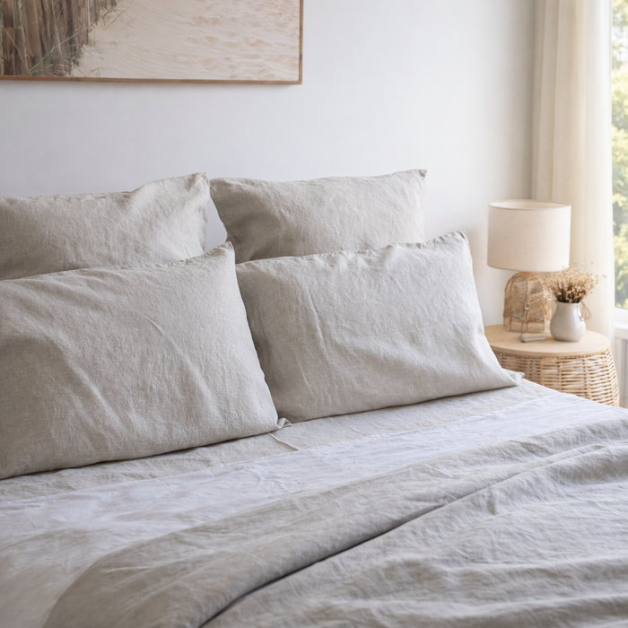 Neatly made bed with light-colored bedding and pillows in a bedroom setting.