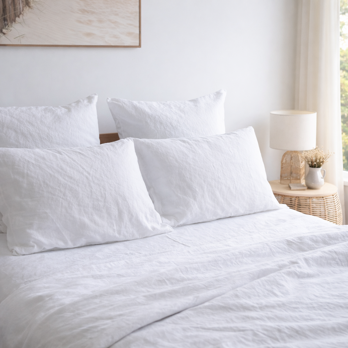 Pure white linen bedding set on a bed with a lamp and decor in the background