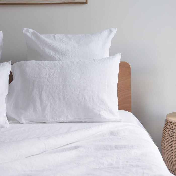 Pure white linen  pillows on a bed with a wooden headboard against a plain wall.