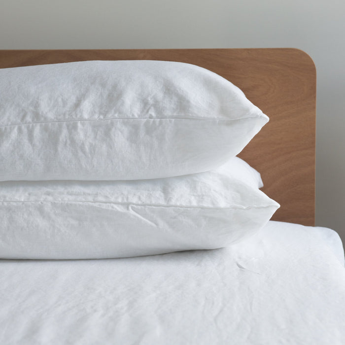 Pure white linen  pillows on a bed with a wooden headboard against a neutral wall