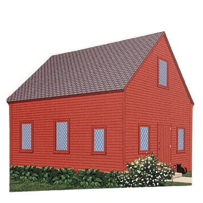 A wooden model of a red Quaker Meeting House with a gray roof, featuring details such as a front door and windows, set against a white background.