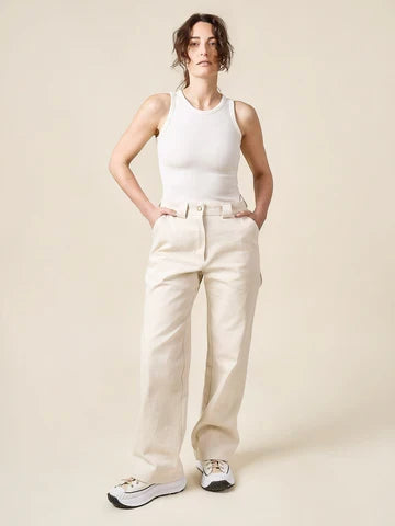 Woman wearing a white tank top and beige pants made of Rika Pants sewing pattern in cropped tailored style with hem cuffs and tabbed waistband  against a plain background
