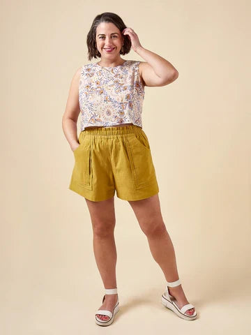 Woman wearing a floral top and yellow shorts made using Sepia Pants and Shorts sewing pattern  against a beige background