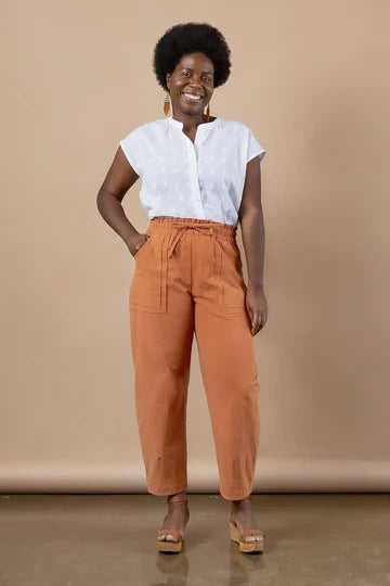 Woman wearing a white blouse and orange pants made using Sepia Pants and Shorts sewing pattern against a beige background