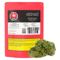 Rear view of a red package labeled "Stöned Super Stoner Selection" with a black-and-white info panel and a cannabis bud positioned in front.
