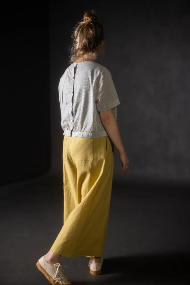 Person wearing a light grey top made using The Celeste Sewing Pattern by Merchant & Mills and yellow pants against a dark background