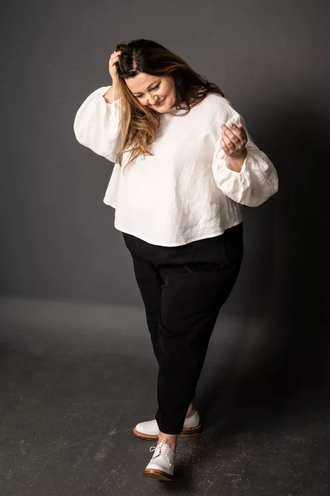 Person wearing a white blouse and black pants against a dark background