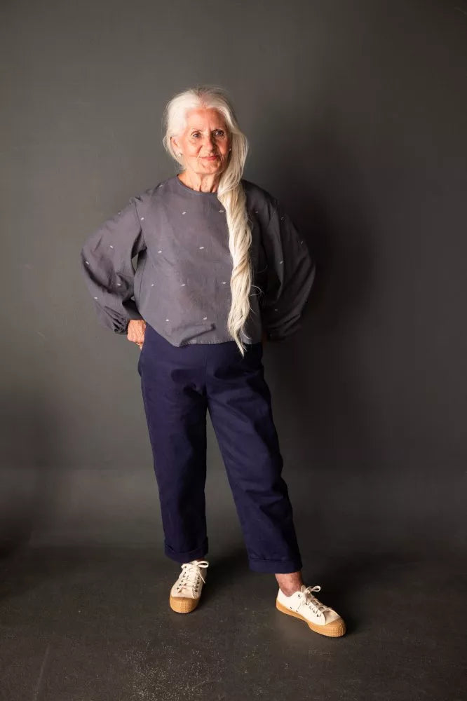 Person wearing a dark sweater and blue pants against a gray background