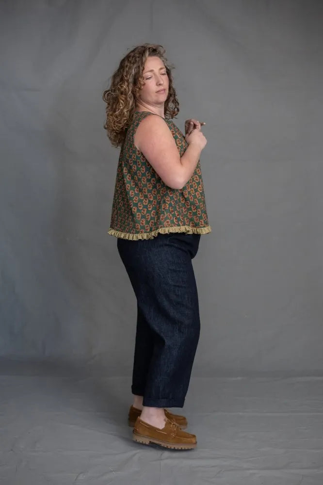 Woman wearing a patterned top and dark pants made using The Eve Trouser Sewing Pattern by Merchant & Mills – cropped tapered trousers with side zip and pleats against a plain background
