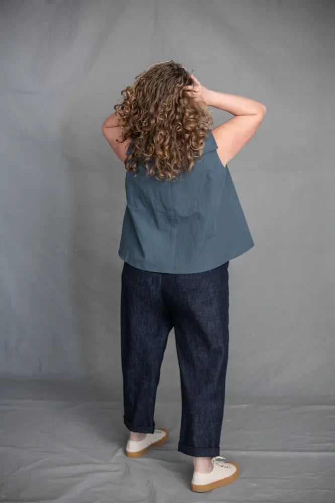 Person wearing a blue top and dark pants  made using The Eve Trouser Sewing Pattern by Merchant & Mills – cropped tapered trousers with side zip and pleats against a gray background