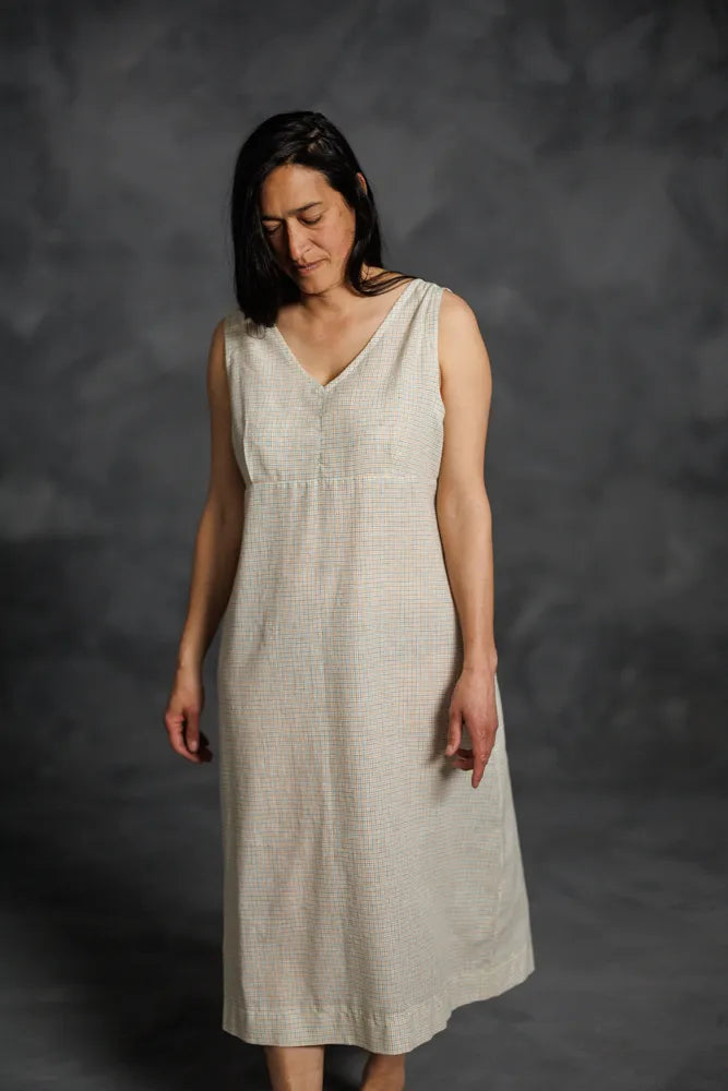 Woman wearing a beige sleeveless dress made using The Lilian Sewing Pattern by Merchant & Mills against a dark background